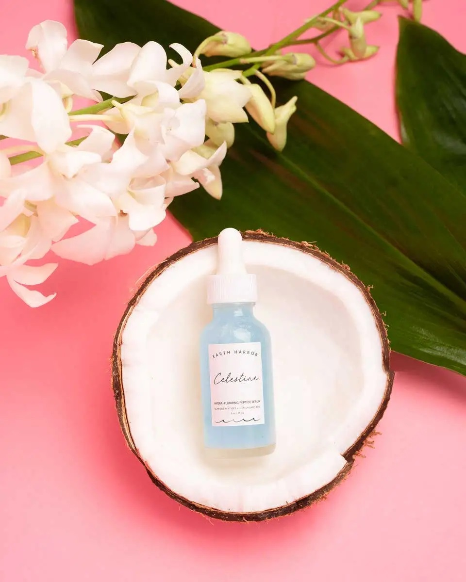 Earth Harbour's Celestine skincare with hyaluronic acid bottle in a coconut on a pink background with a decorative plant leaf