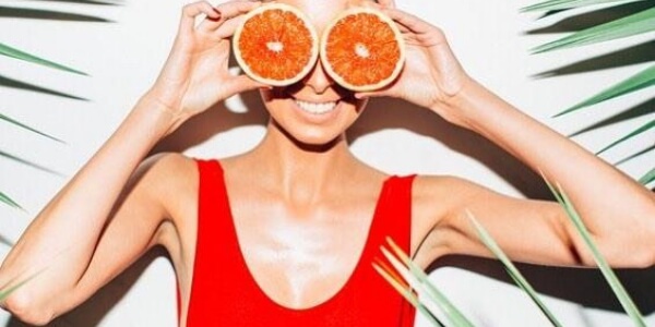 A woman holding oranges over her eyes.